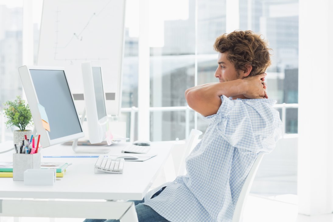 Side view of a casual young business man using computer in a bright office arched back
