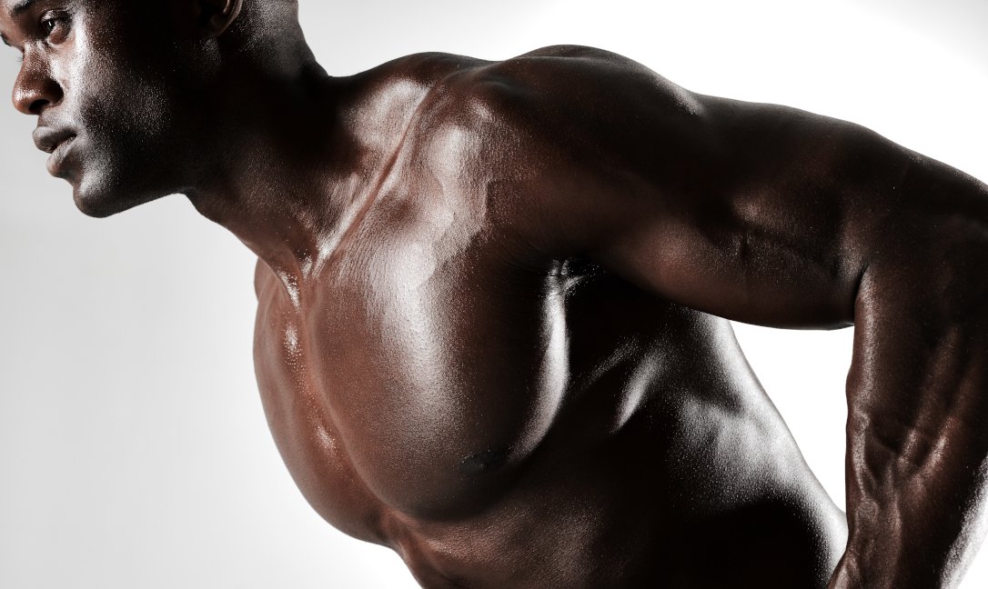 Close up of masculine young african male performing rear deltoid row against grey background. Bodybuilder with muscular physique.