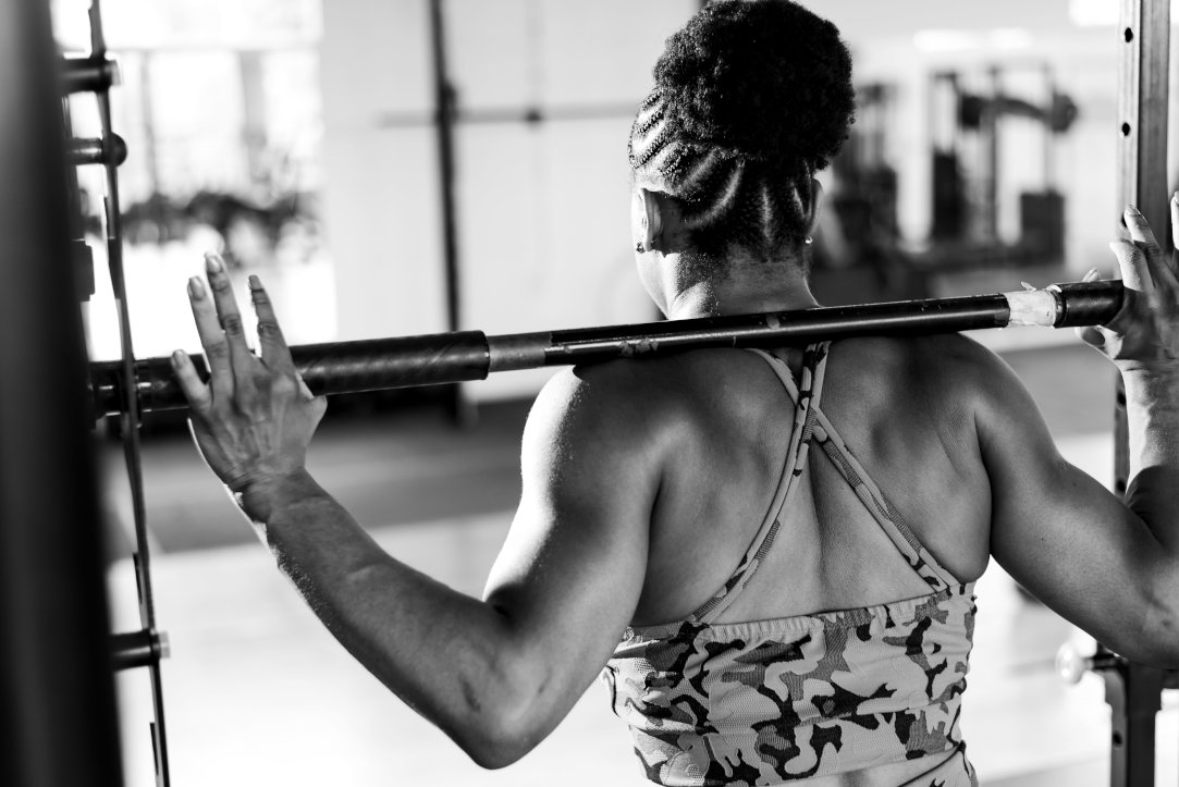 A black and white photograph of a female athlete performing compound movements back in a gym
