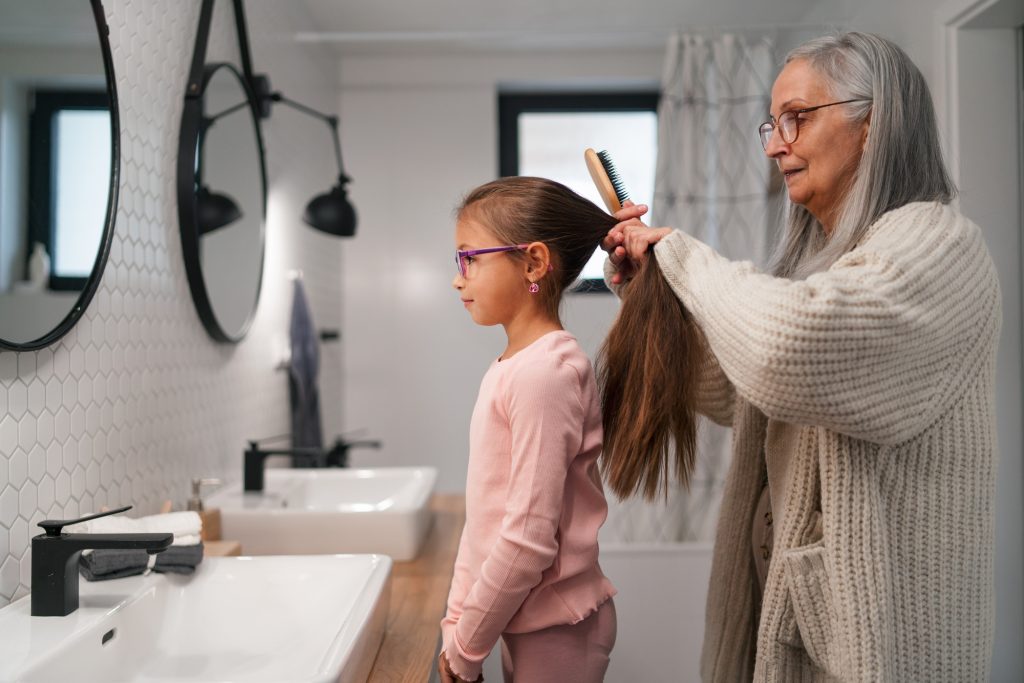 Senior grandmother and granddaughter standing indoors in bathroom, daily routine concept.